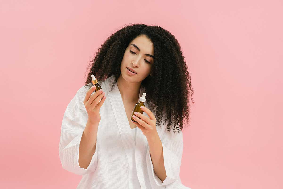 A woman in a white robe examines two skincare serums, contemplating which brand truly delivers the best results—because not all skincare is created equal.