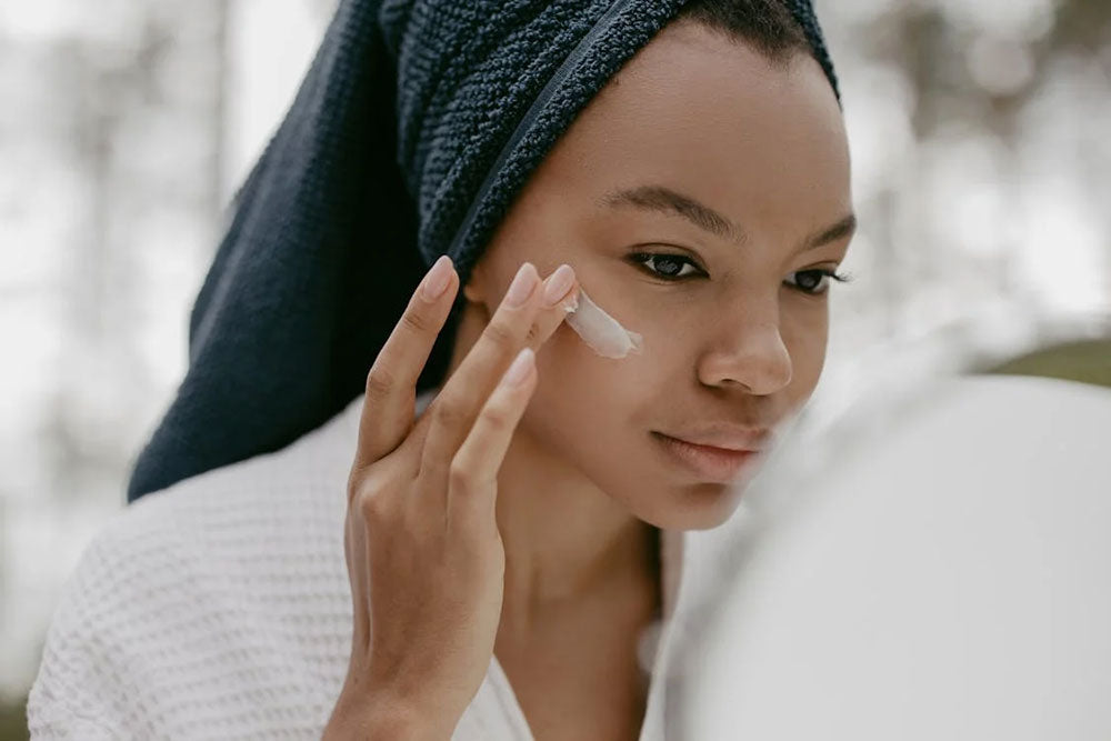 A woman applying lotion to her face, representing skincare routines while exploring the science of exfoliation and pH balancing with Lotion P50.