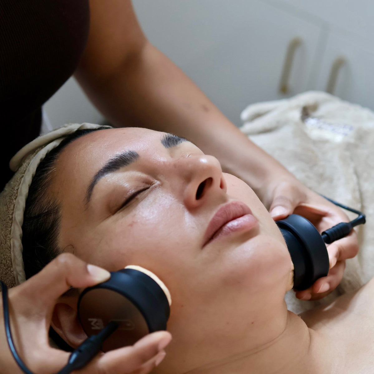 Person receiving a facial treatment with microcurrent devices on a neutral background