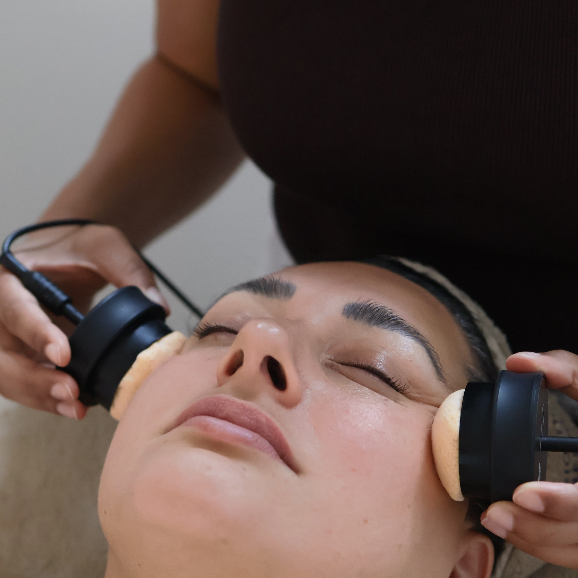 Person receiving a facial treatment with Bio Visage microcurrent device on a neutral background